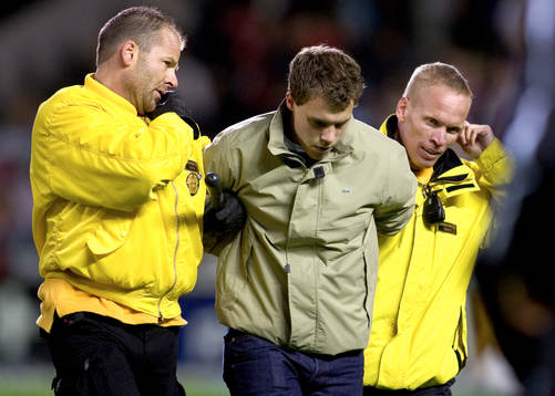 Supportern som stormade planen tas omhand av vakterna.