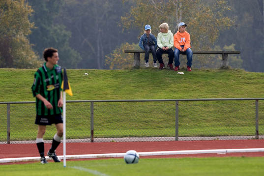 Tre unga supportrar. Bänk. Idyllisk idrottsplats