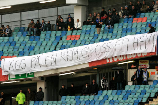Banderoll, "Lägg på en rem, ge oss ett hem", läktare