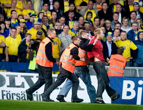 Vakter släpar bort en huligan som sprungit in på läktaren