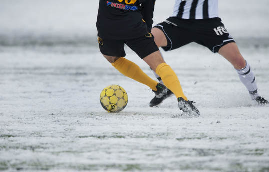 Fot, fotboll, fotbollsskor. Snö, snöig konstgräsplan.