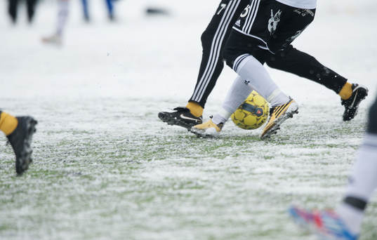 Fot, fotboll, fotbollsskor. Snö, snöig konstgräsplan.