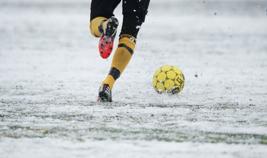 Fot, fotboll, fotbollsskor. Snö, snöig konstgräsplan.