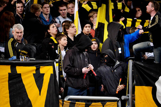 Maskerade personer i AIK-klacken med bengaler innan matchen