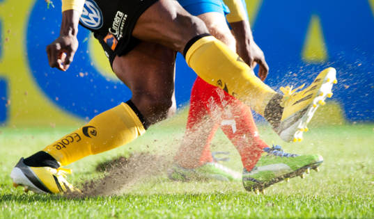 Fot, fotbollsskor, gräs som yr, sand i gräset