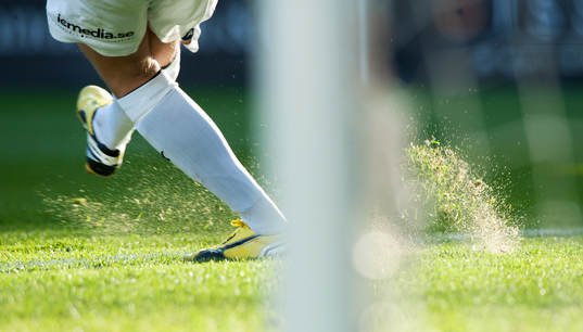 Fot, fotbollsskor, gräs som yr, målstolpe