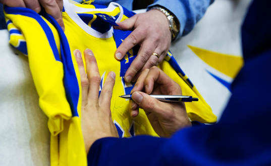 En spelare skriver sin autograf på en matchströja