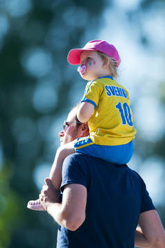 Liten svensk supporter på pappas axlar och med napp i mun