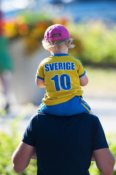Liten svensk supporter på pappas axlar och med napp i mun