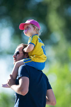 Liten svensk supporter på pappas axlar och med napp i mun