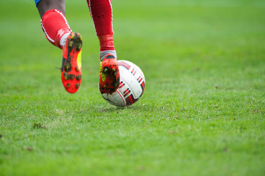 Fotbollsskor, dubbar, fot, gräs och boll i matchen i