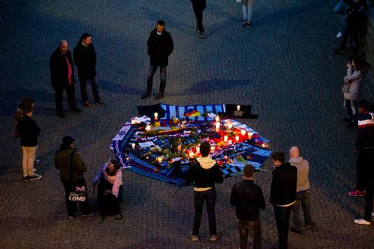 Personer sörjer vid tända ljus och utlagda halsdukar och