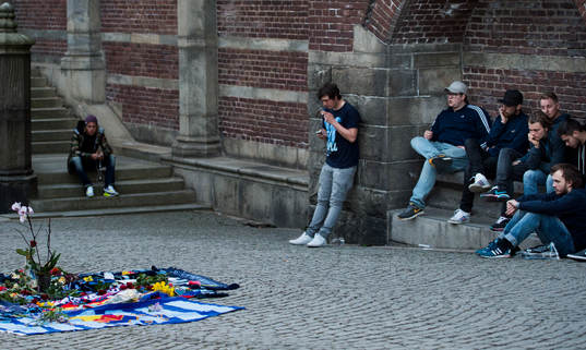 Personer sörjer vid tända ljus och utlagda halsdukar och