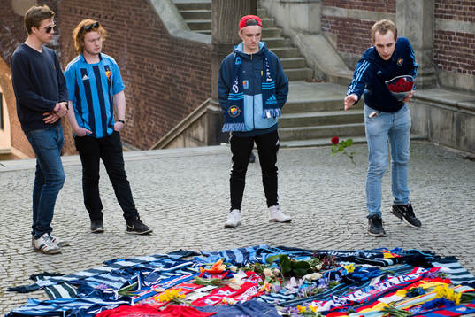 Personer sörjer vid tända ljus och utlagda halsdukar och