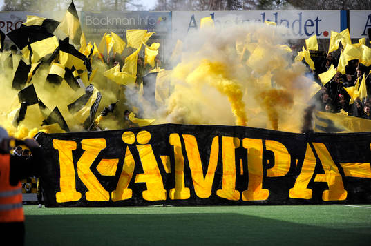 AIK-flaggor och rök  samt banderoll med texten "kämpa"