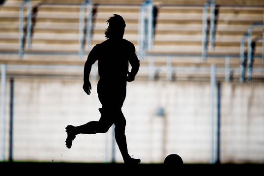 En fotbollsspelare med boll i siluett
