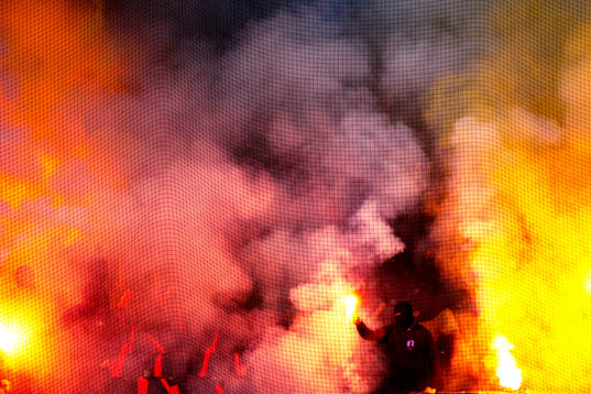 En maskerad Djurgårdssupporter håller i en bengal
