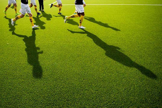 Skuggor av fotbollsspelare som värmer upp på konstgräs