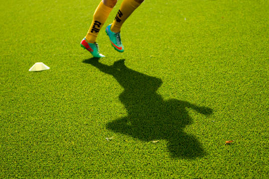 Skugga av en fotbollsspelare som värmer upp på konstgräs