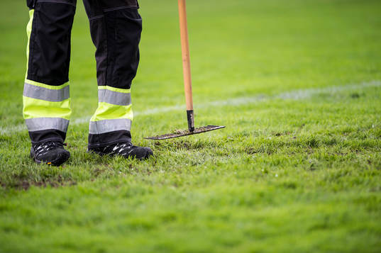 Vaktmästare plattar till gräset med kratta innan innan