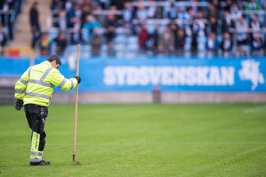 Vaktmästare plattar till gräset med kratta innan innan