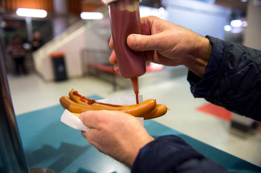 En person tar ketchup på korv med bröd innan en