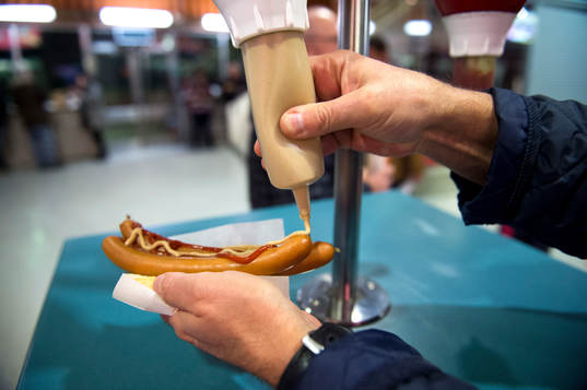 En person tar senap på korv med bröd innan en