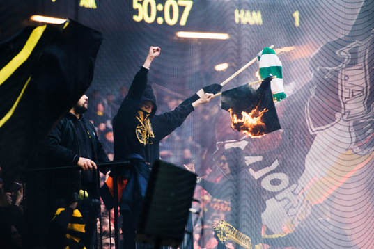 Några AIK supportrar bränner en Hammarby flagga