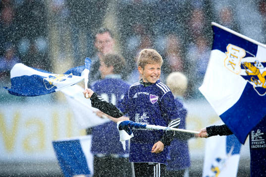 En kille viftar med en flagga innan en fotbollsmatch i