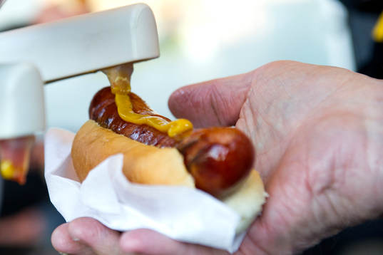 En person tar senap på en korv med bröd