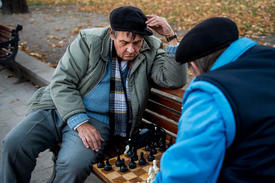 Två äldre herrar spelar schack på en parkbänk en