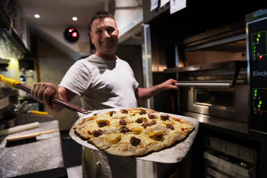 Pizzabagaren Philippe Kervella håller upp en pizza kallad