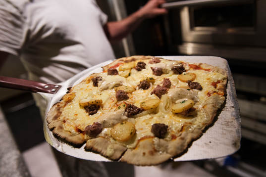 Pizzabagaren Philippe Kervella håller upp en pizza kallad