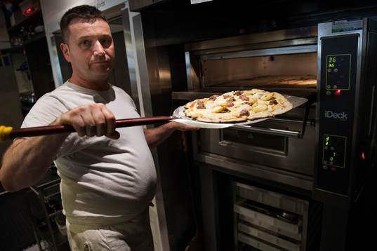Pizzabagaren Philippe Kervella håller upp en pizza kallad