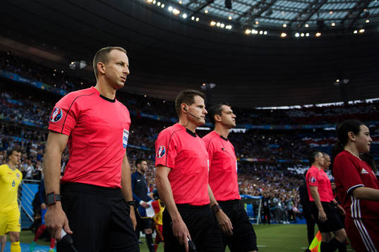 Domare Viktor Kassai med sitt team går in på arenan