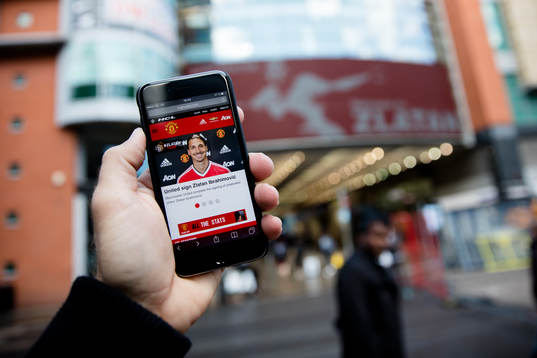En man läser United nyheter på mobilen