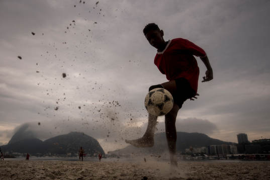Pojke trixar med en fotboll på stranden