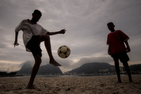 Pojkar trixar med en fotboll på stranden