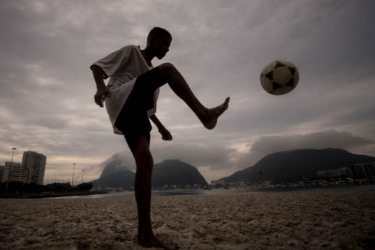 Pojke trixar med en fotboll på stranden
