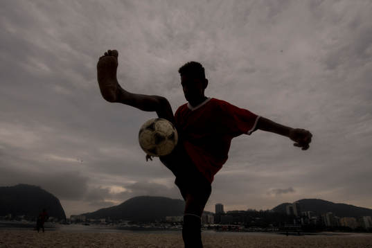 Pojke trixar med en fotboll på stranden