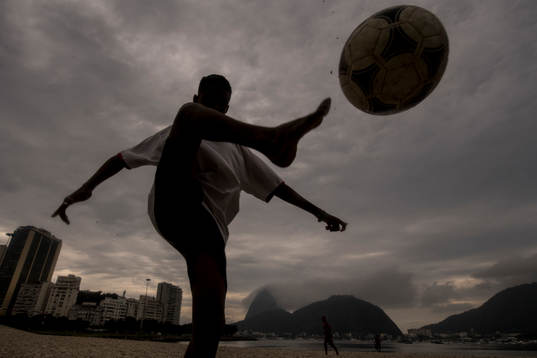 Pojke trixar med en fotboll på stranden
