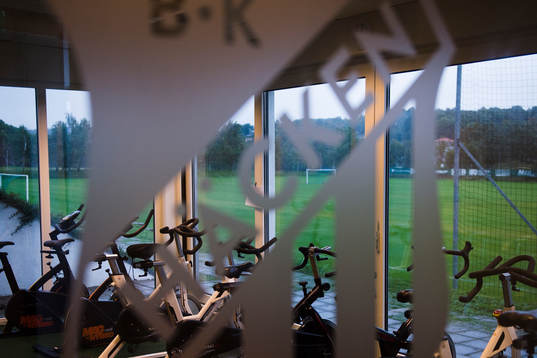 Häckens klubbmärke framför ett rum med motionscyklar på