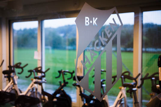 Häckens klubbmärke framför ett rum med motionscyklar på