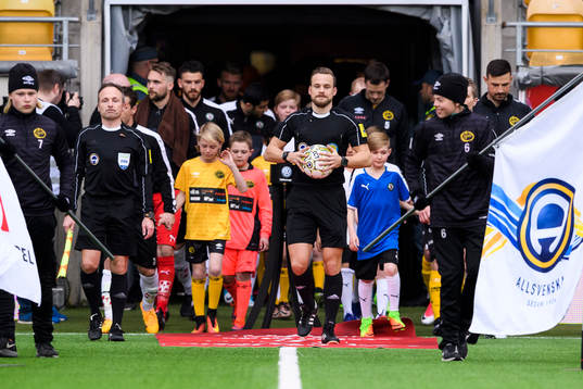 Domare och spelare kommer in till match med Domare