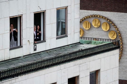 Tre personer står i ett fönster vid Sergels torg när