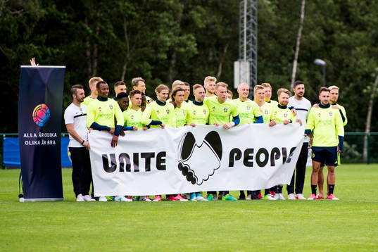 Laget fotograferas bakom en banderoll Unite People