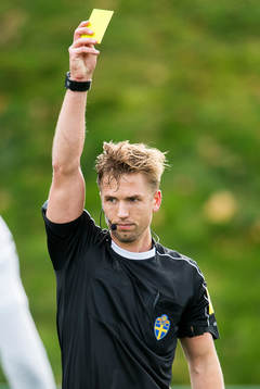 Matchens domare Fredrik Hansson visar det gula kortet