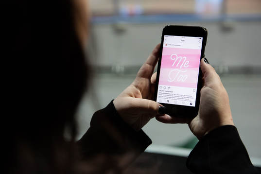 En kvinna kollar på sin mobil med visandes en #metoo bild