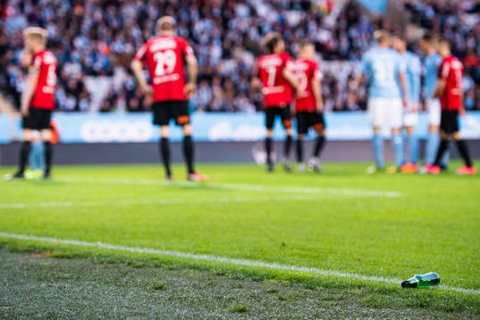 En inkastad ölflaska ligger vid planen