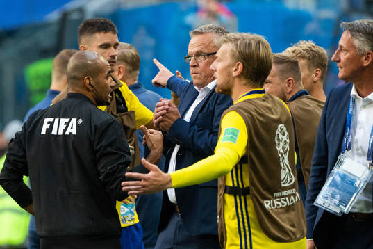 A referee talks with head coach Janne Andersson of Sweden